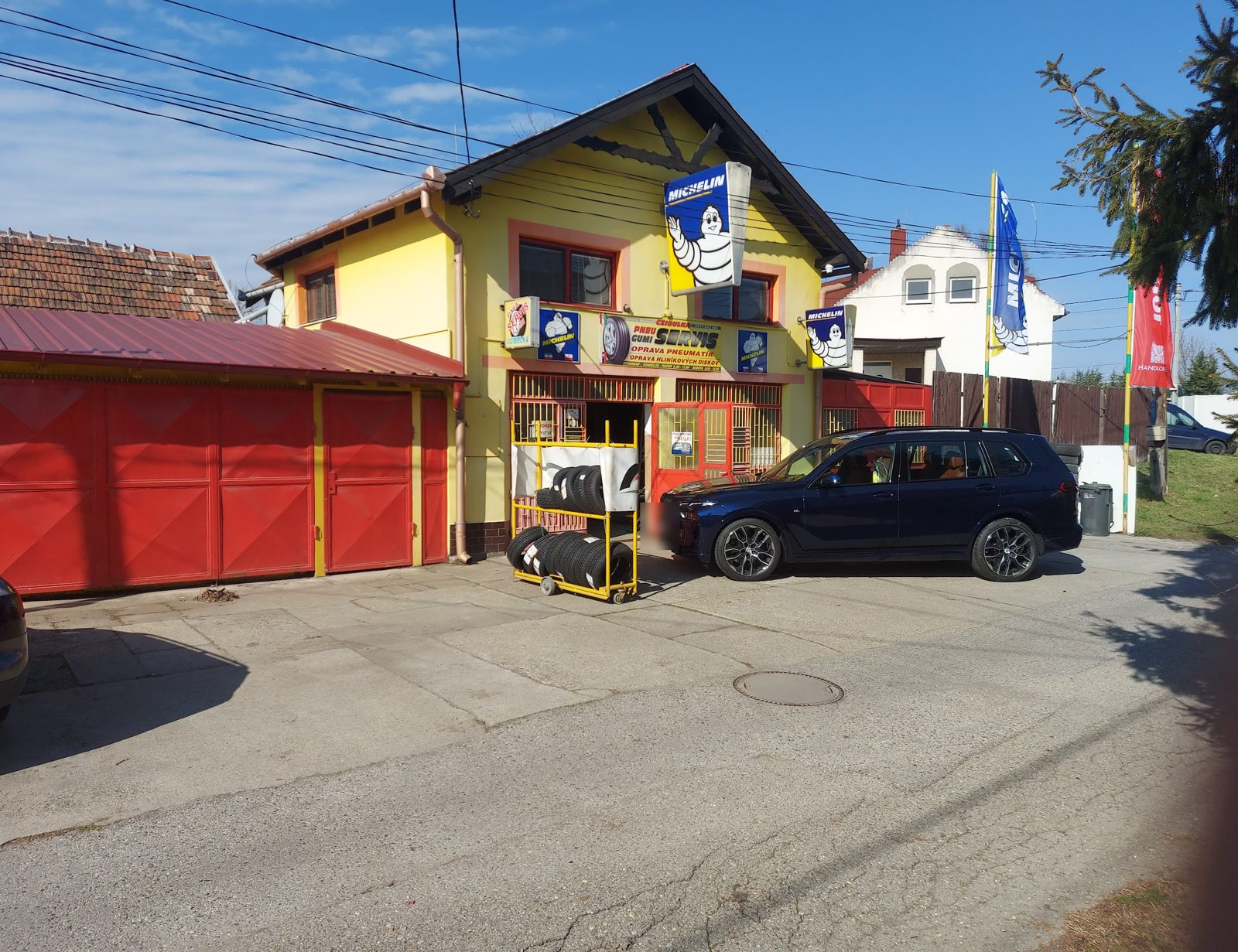 Dielňa Pneuservis Czibulka na Bažantii 13: žltý dom, červené garážové brány a stojan s pneumatikami pred vchodom